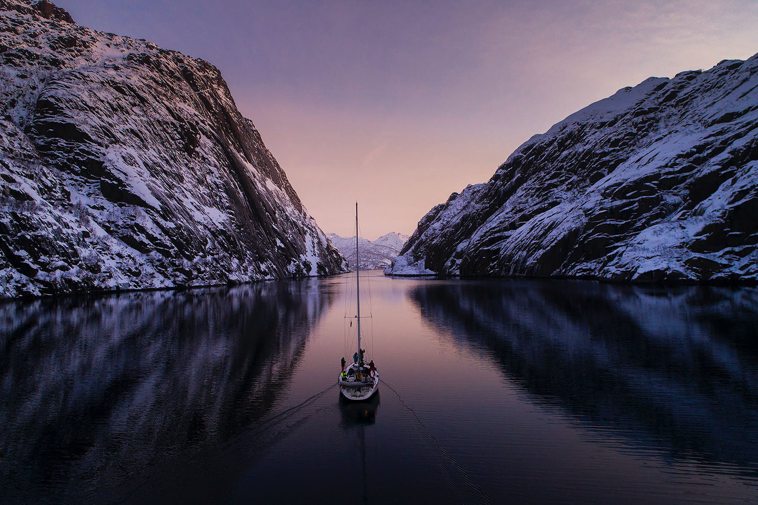 Voilier naviguant dans les fjords norvégiens enneigés lors des lumières hivernales et se dirigeant au mouillage lors de la Croisière scientifique à la voile sur les orques et baleines à bosse de Norvège -copyright SailNorway